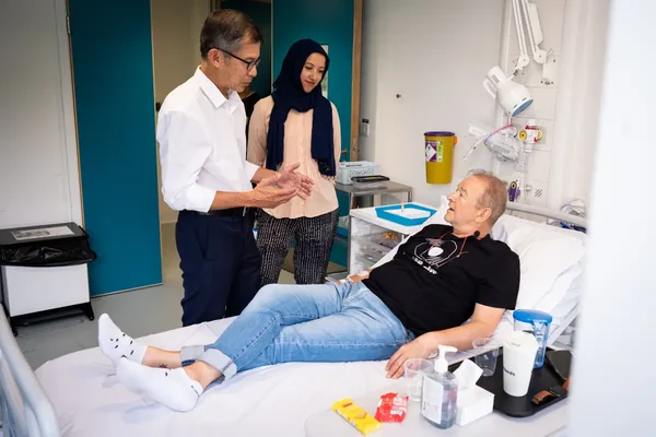 Un patient allongé dans un lit d'hôpital discutant avec un médecin et une femme voilée lors des premiers essais du vaccin contre le cancer du poumon utilisant la technologie à ARN messager du Covid-19