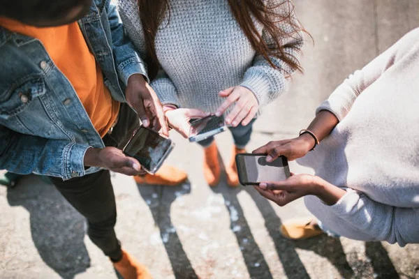 Groupe de jeunes adolescentes utilisant des smartphones à l'extérieur, illustrant l'usage des réseaux sociaux par les jeunes