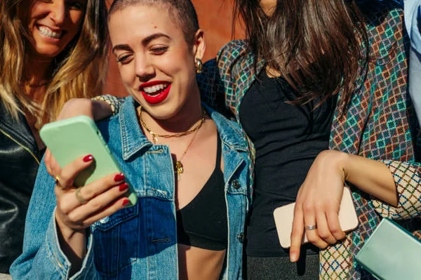 Trois jeunes femmes dans un cadre urbain lumineux, regardant leurs smartphones, illustrant l'engagement des jeunes avec les plateformes numériques