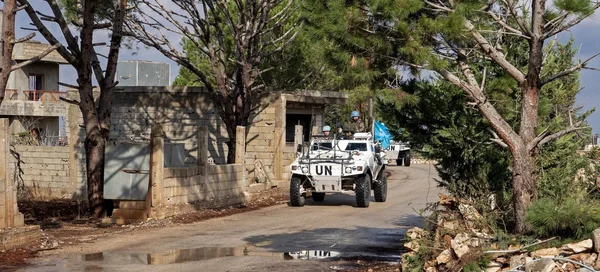 Un véhicule blindé blanc des Nations Unies avec des casques bleus circulant sur une route de terre dans le sud du Liban, passé des bâtiments en béton endommagés