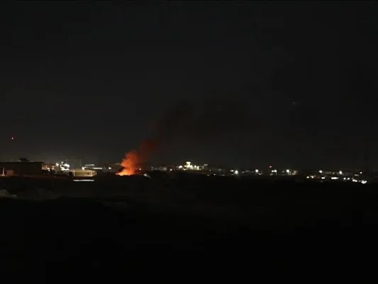Vue nocturne d'une explosion avec des flammes orange et de la fumée s'élevant au-dessus de l'installation de la base près de l'aéroport de Bagdad lors d'une attaque par drone.