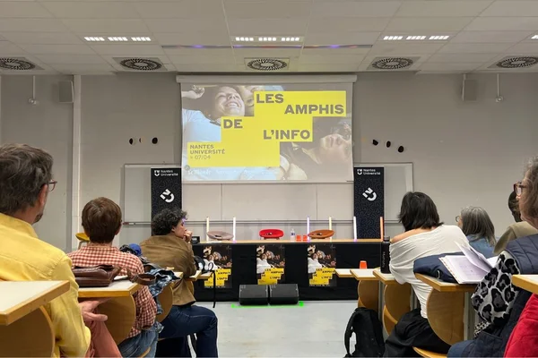 Salle d'amphithéâtre lors des Amphis de l'Info à Nantes Université, avec un public d'étudiants face à un écran de projection affichant le titre de l'événement