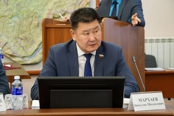 Le député russe Vyacheslav Markhaev, membre du Parti communiste, en costume bleu assis à son bureau avec une plaque portant son nom