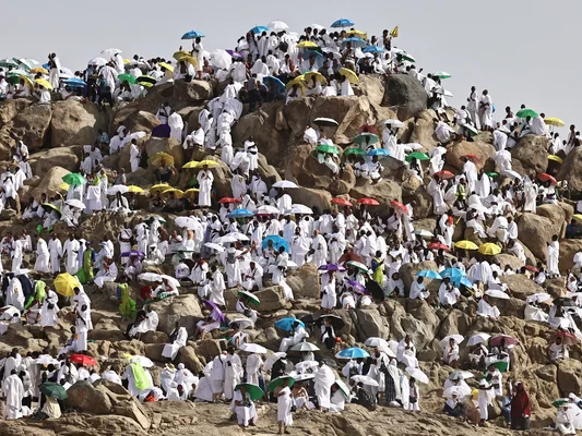 Foule de pèlerins du Hajj réunis sur le mont Arafat sous un soleil de plomb, beaucoup tenant des parapluies colorés pour se protéger