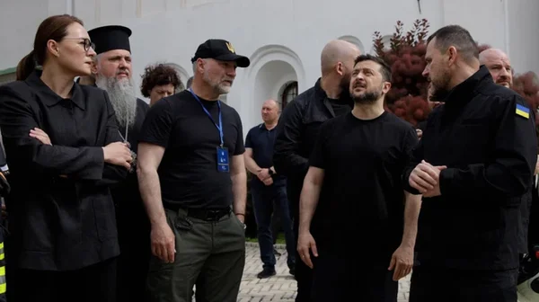Volodymyr Zelenskyy en t-shirt noir visitant le monastère endommagé de Kyiv après l'attaque russe, entouré d'officiels ukrainiens