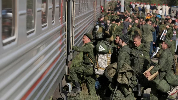 Soldats en uniforme de camouflage vert montant dans un train de voyageurs argenté avec de gros sacs à dos et du matériel militaire