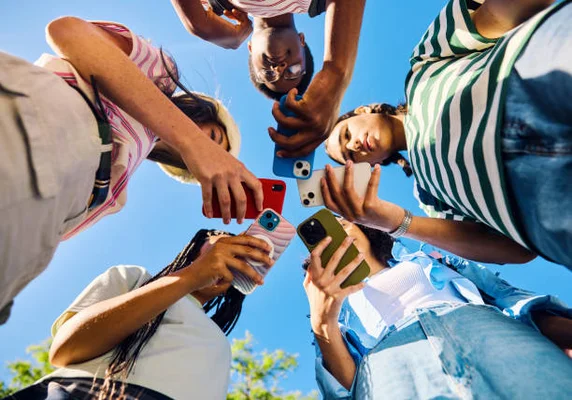 Groupe de jeunes adultes de la génération Z ensemble à l'extérieur, tous concentrés sur leurs téléphones, symbolisant la connexion numérique des adolescents