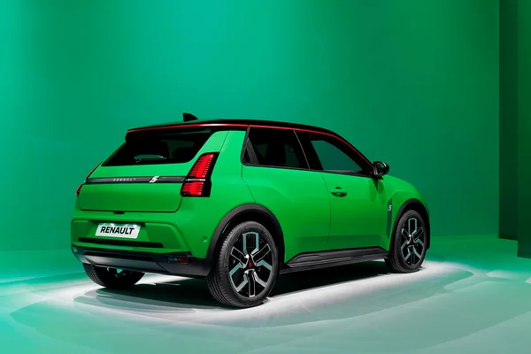 Renault 5 électrique verte vif en vue arrière trois-quarts sur fond vert assorti, avec toit noir et ligne d'accent rouge, jantes en alliage géométriques et passages de roue noirs