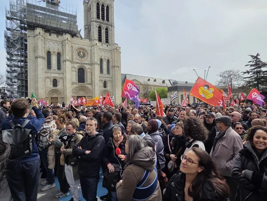 Manifestation antiraciste à Saint-Denis en soutien à Bally Bagayoko, avec une foule diverse devant une église en rénovation, tenant des drapeaux rouges et violets.