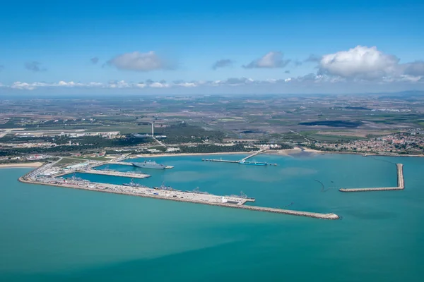 Photographie aérienne de la station navale de Rota, grand port industriel avec quais, brise-lames et plusieurs navires dans un port par jour ensoleillé.