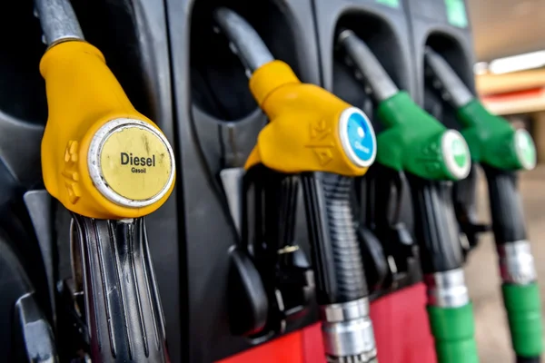 Vue de pistolets de distribution de carburant dans une station-service : un pistolet jaune labellisé 'Diesel / Gasoil' à l'avant-plan, entouré de pistolets verts et bleus, dans le contexte de la hausse des prix due à la guerre au Moyen-Orient.
