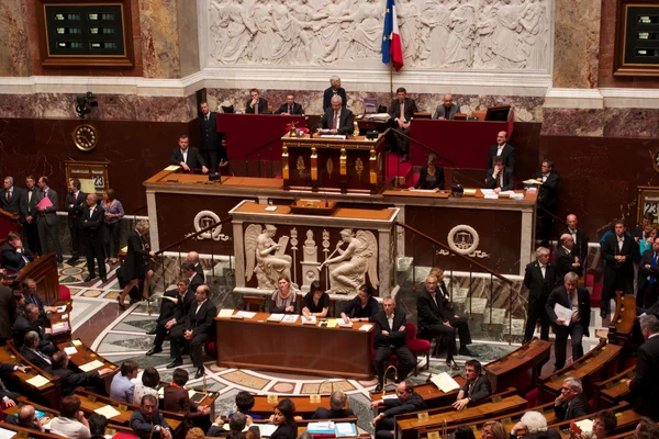 Claude Bartolone au perchoir de l'Assemblée nationale, entouré de députés en tenue formelle dans un hémicycle orné de colonnes de marbre et du drapeau français, lors du vote de la loi sur le mariage pour tous.