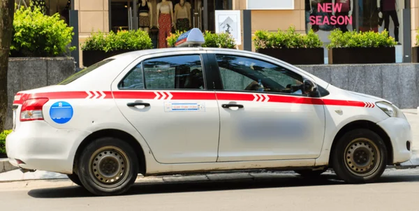 Taxi de l'aéroport de Hanoï, véhicule blanc avec bande rouge et luminaire de toit, stationné dans une rue urbaine devant une boutique affichant 'NEW SEASON'.