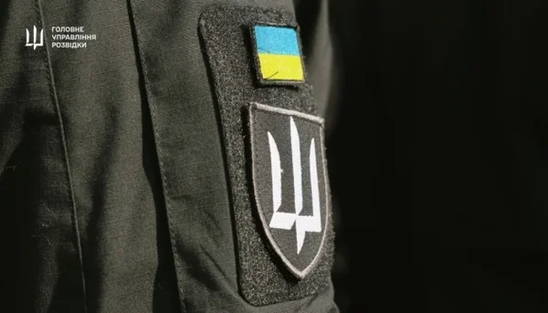 Gros plan sur la manche d'un uniforme militaire ukrainien avec patch drapeau et bouclier au trident, logo du renseignement militaire ukrainien, lié à un article sur une cyberattaque.