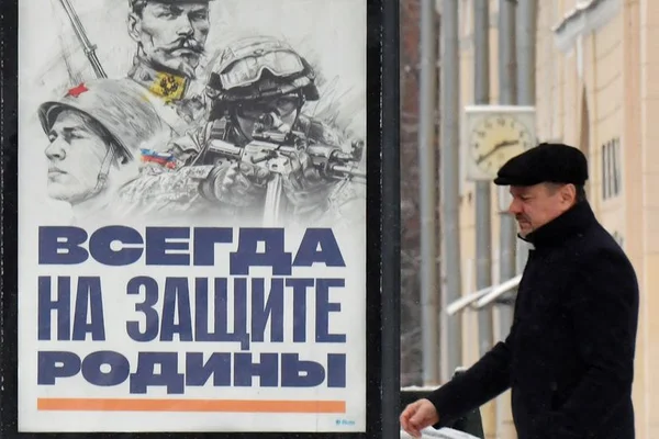 Article de La Dépêche sur la campagne de recrutement militaire russe : un homme en manteau et casquette noirs passe devant un poster de soldats avec le texte russe 'Toujours au défens de la Patrie'.