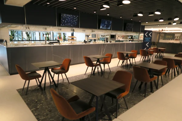 Bar du secteur hospitalité du Tottenham Hotspur Stadium, situé au troisième étage, avec comptoir moderne, verrerie suspendue, tables et chaises orange, plafond sombre et éclairage sur rails.