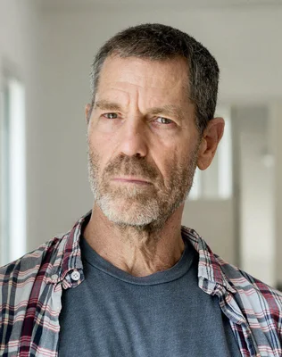 Ohad Naharin lors d'une répétition publique du Ballet du Rhin : gros plan sur un homme d'âge moyen aux cheveux grisonnants et à la barbe, portant une chemise à carreaux sur un t-shirt gris.