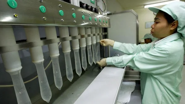 Article TF1 Info sur la pénurie de préservatifs liée au coronavirus : ouvrier en uniforme vert clair, coiffe et gants manipulant une machine de fabrication.