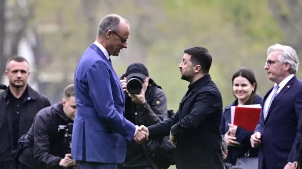 Volodymyr Zelensky en veston noir et Friedrich Merz en costume bleu se serrant la main à l'extérieur, entourés de photographes, lors d'une déclaration sur l'innovation de l'industrie de défense ukrainienne.