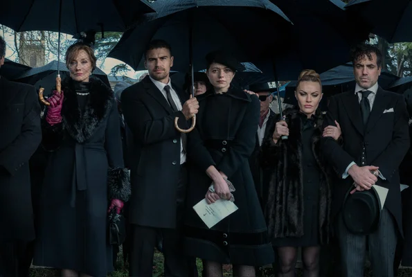 Scène de la série The Gentlemen (2024) de Guy Ritchie : groupe de personnes en tenue noire formelle tenant des parapluies, réunies en extérieur lors d'un enterrement ou mémorial.