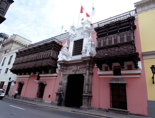 Le Ministère des Affaires étrangères du Pérou, bâtiment colonial de Lima à façade rose ornée de balcones en bois sombre, drapeaux péruviens sur le toit et entrée baroque en pierre.