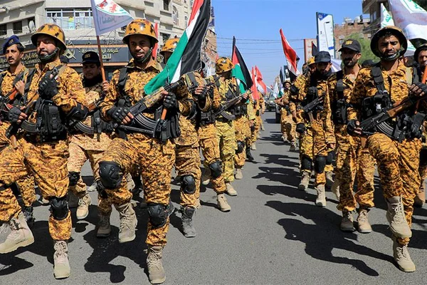 Des soldats rebelles houthis du Yémen en uniforme de camouflage désertique, armés de fusils et portant des drapeaux, marchent en formation dans une rue, suite à l'affirmation de leur chef de poursuivre les attaques contre Israël.
