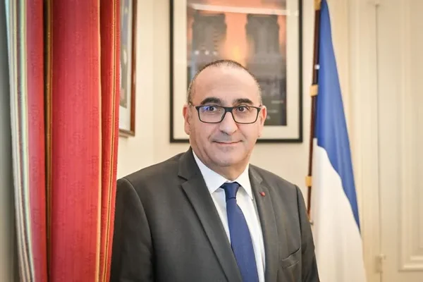 Laurent Nuñez, nommé ministre de l'Intérieur selon Le Berry Républicain, en costume gris, cravate bleue et lunettes, debout entre un rideau rouge et un drapeau français en intérieur officiel.
