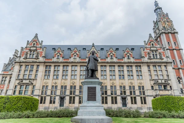 L'université libre de Bruxelles, vue d'un grand bâtiment en brique orné avec une tour horloge et une statue d'un homme sur un piédestal au premier plan.