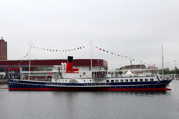 Le bateau à vapeur Princess Elizabeth, bleu et blanc à cheminée rouge, amarré en tant que restaurant au port de Dunkerque sous un ciel couvert, avec fanions et arrière-plan urbain.