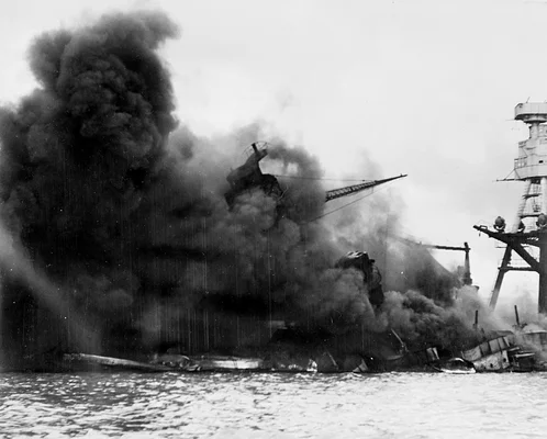 Photographie historique en noir et blanc d'un grand navire de guerre en flammes et enveloppé de fumée noire, arrosé d'eau lors d'un désastre naval, utilisée pour illustrer le sujet des armes chimiques immergées abordé par Ouvry.