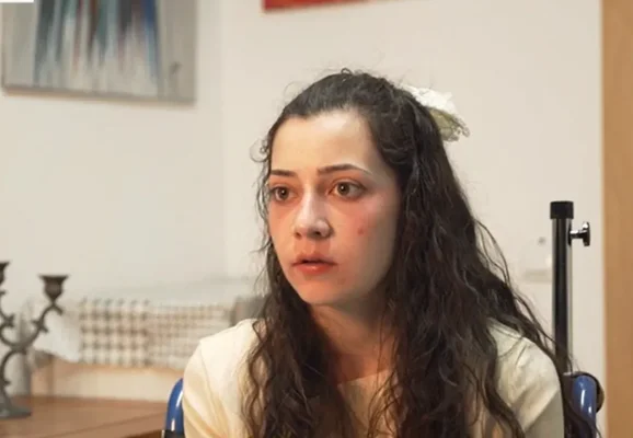 Jeune femme aux cheveux longs et ondulés portant une fleur blanche, expression sérieuse, image vidéo issue d'un reportage sur l'euthanasie d'une Espagnole de 25 ans relançant le débat fin de vie.
