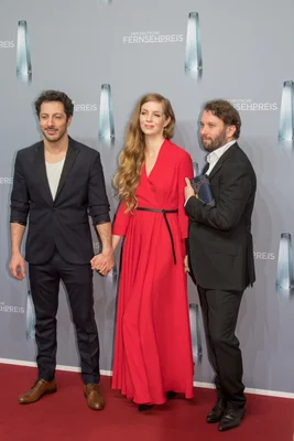 Fahri Yardım, Pheline Roggan et Christian Ulmen posant ensemble sur le tapis rouge devant un décor indiquant 'DER DEUTSCHE FERNSEHPREIS' lors du Deutscher Fernsehpreis 2018.