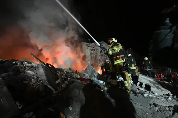 Guerre en Ukraine : pompiers en tenue de protection arrosant un grand incendie parmi les débris d'un immeuble détruit à Kharkiv lors de bombardements nocturnes ayant fait des morts.