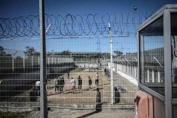Vue d'un centre de rétention administrative depuis un grillage métallique surmonté de fils barbelés, montrant un groupe de personnes dans une cour extérieure sécurisée, lors d'un reportage de RTL.