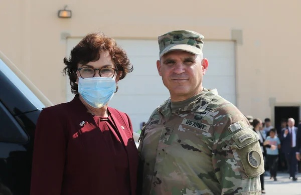 Lors d'une visite de membres du Congrès américain à Camp As Sayliyah au Qatar, une femme en blazer bordeaux et masque bleu aux côtés d'un soldat en tenue de camouflage pose devant un bâtiment beige, novembre 2021.