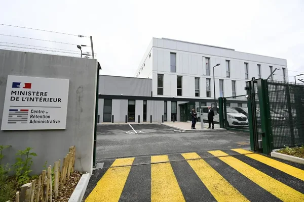 Façade du Centre de rétention administrative près d'Orléans, bâtiment blanc moderne avec panneau du Ministère de l'Intérieur, portail vert et ralentisseur à bandes jaunes et noires, suite à un rapport sur les conditions de vie.