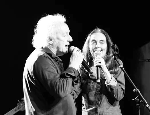 Photographie en noir et blanc de Didier Barbelivien, parolier français, et de Régine Hantelle en concert à Reims : un homme aux cheveux blancs bouclés et une femme aux longs cheveux sombres chantant dans des microphones sur scène.
