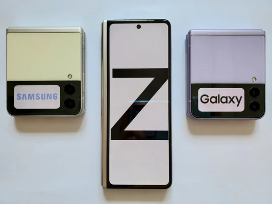 Photographie de smartphones pliables Samsung Galaxy Z Flip et Z Fold : trois appareils Z Flip sur une surface blanche, celui du centre déplié affichant un grand 'Z', les deux autres fermés.