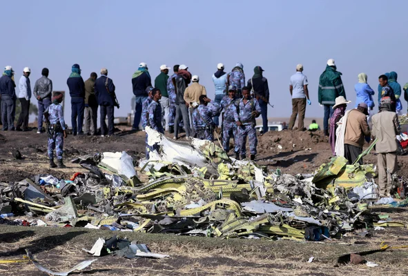 Scène du crash du Boeing 737 MAX en Éthiopie : des agents de sécurité et des civils se tenant près d'un grand amas de débris métalliques tordus dans un champ ouvert sous un ciel clair, suite aux conclusions de l'enquête contestées par des experts américains.