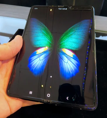 Main tenant un smartphone pliable Samsung Galaxy Fold déplié, affichant un fond d'écran vibrant représentant un papillon.