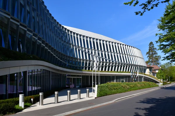 Le siège du Comité international olympique (Maison olympique) à Lausanne, façade de verre courbe à design ondulant avec ailettes verticales, anneaux olympiques en arrière-plan.