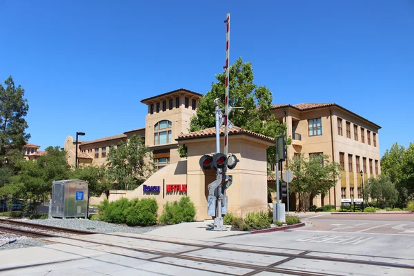 Ancien siège de Netflix au 100 Winchester Circle à Los Gatos, Californie, avec passage à niveau à l'avant-plan et grand bâtiment beige arborant les logos Roku et Netflix sous un ciel bleu clair.