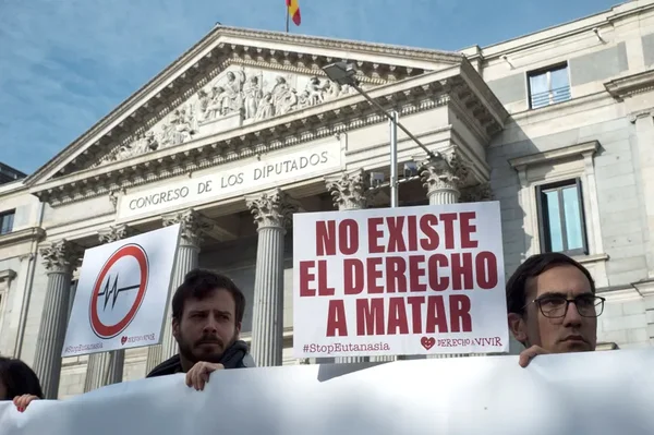 L'Espagne a dépénalisé l'euthanasie : manifestants devant le Congrès des députés espagnol tenant des pancartes 'NO EXISTE EL DERECHO A MATAR' et un symbole de battement de cœur barré.