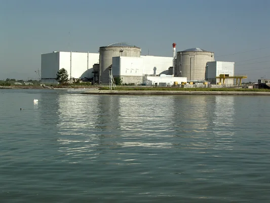 Vue de la centrale nucléaire de Fessenheim (Haut-Rhin, Alsace, France) avec deux dômes de confinement et bâtiments adjacents, située en bord de rivière ou canal sous ciel dégagé.