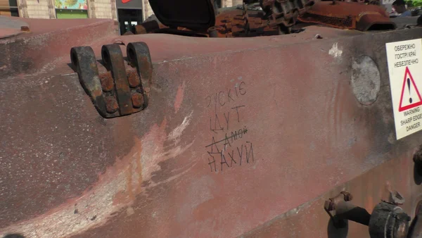 Gros plan sur la surface métallique rouillée et rougeâtre d'un véhicule militaire russe détruit exposé à Kiev pour la fête de l'Indépendance, avec graffiti cyrillique et autocollant d'avertissement.