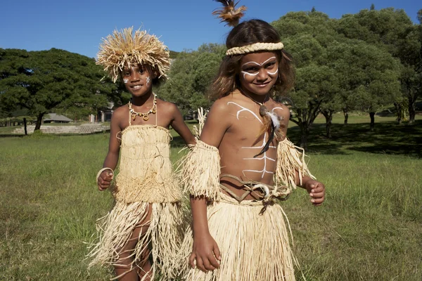 Image de voyage en Nouvelle-Calédonie présentée par Voyage Unique : deux enfants en jupes de herbe et peinture corporelle dans un champ herbeux avec arbres.