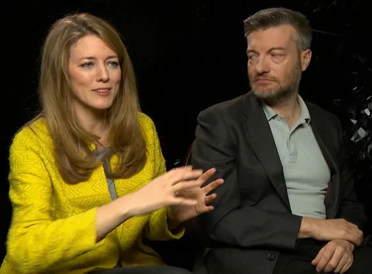 Charlie Brooker, créateur de Black Mirror, et Annabel Jones, productrice, en interview chez MTV UK : la femme blonde en pull jaune parle en gesticulant, l'homme barbu en blazer sombre l'écoute.