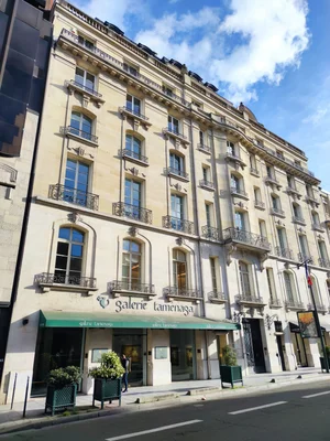 Le 18, avenue Matignon dans le 8e arrondissement de Paris : vue extérieure d'un immeuble de plusieurs étages à façade de pierre classique, avec une marquise verte de la Galerie Tamenaga, des fenêtres à balcons en fer et une personne près de l'entrée.