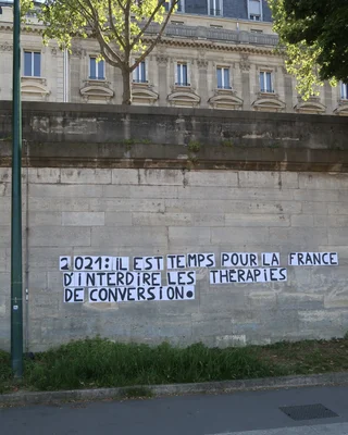 Photographie d'un mur en pierre sur la promenade des Berges-de-la-Seine-André-Gorz à Paris, affichant un message pochoiré : "2021 : il est temps pour la France d'interdire les thérapies de conversion".