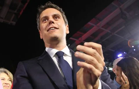 Personnalité du mouvement Renaissance en costume sombre et cravate bleue, applaudissant avec un sourire et regardant vers le haut devant d'autres personnes, dans le contexte de la primaire présidentielle.